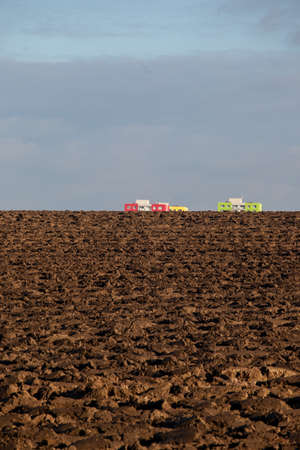 Two apartment buildings, green, red and yellow, seem to rise from the ground. The field was recently plowed. The impression is funny and surprising.の写真素材