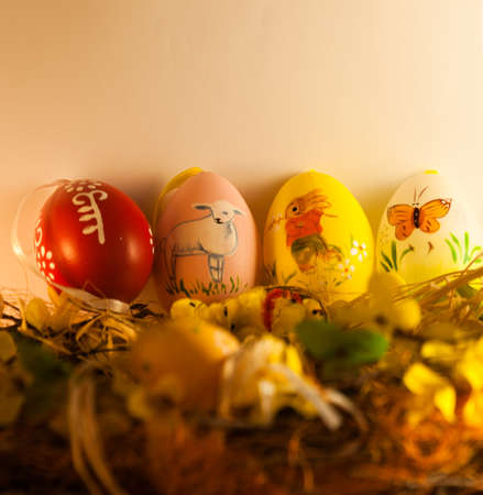 Four different colored Easter eggs with animals are placed on a decorated wreath. There is a rabbit, a lamb and a butterfly.の写真素材
