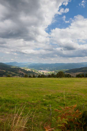 The sky is overcast and a little blue. A large green meadow slopes down to the valley. In the distance another massive stands out.の写真素材