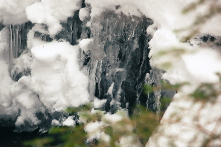 The water of the small waterfall froze forming abstract patterns. This is framed by snow and shrub...