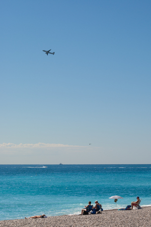 Promenade des anglais, Nice, France - September 2012 : Tourists on the pebble beach and a plane taking off.のeditorial素材
