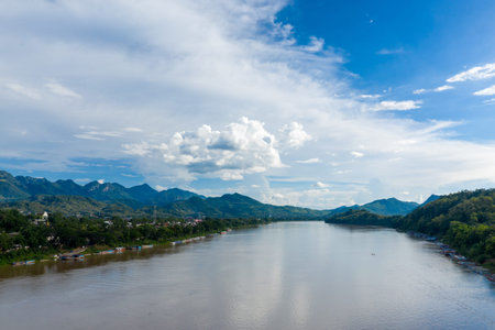 The Mekong River flows between lush green hills and the riverside town of Luang Prabang, Laos....