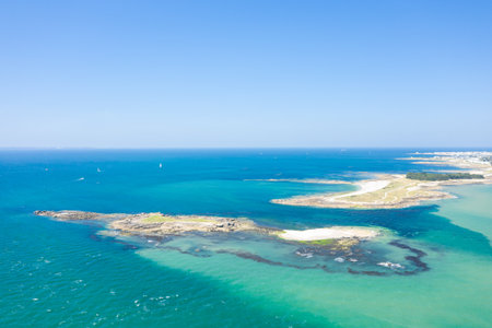 Aerial view of sunlit islets and winding sandy paths surrounded by vibrant turquoise water near Quiberon. The clear blue sky and open sea create a bright, inviting atmosphere.の写真素材
