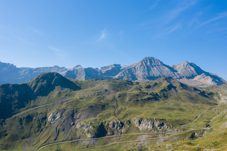 Sweeping view of sunlit grassy hills and dramatic rocky mountains near Gavarnie Gedre in the French Pyrenees. Clear blue sky enhances the sense of vast open space and natural grandeur.の写真素材