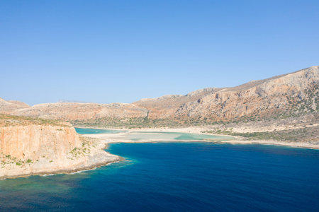 Expansive view of Balos Beach in Crete, Greece, featuring a vivid turquoise lagoon bordered by steep...