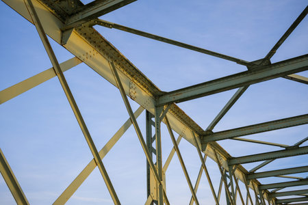 Close-up view of geometric metal beams forming the framework of an iron bridge, highlighted by soft...