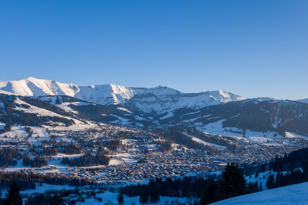Wide panoramic view of Megeve village surrounded by snow-blanketed hills and dramatic sunlit...