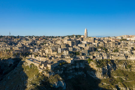 Sunlit panorama of Matera, Italy, displaying a dense array of historic stone houses cascading along...
