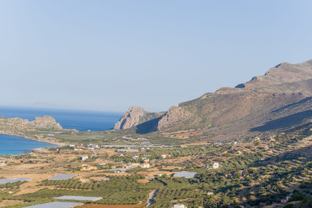 Expansive olive groves and scattered greenhouses stretch across the sunlit coastal plain near...