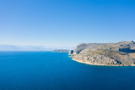 Expansive aerial scene of a rugged rocky peninsula jutting into deep blue water, with distant hazy...