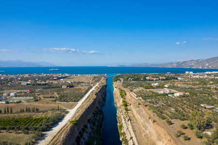 Aerial view of the Corinth Canal cutting through rural farmland and olive groves, leading to the deep blue sea with distant mountains under a clear sky.の写真素材