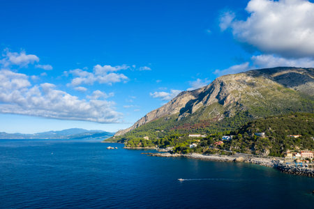 Steep mountains covered in green vegetation descend to a rugged shoreline, with deep blue sea and a...