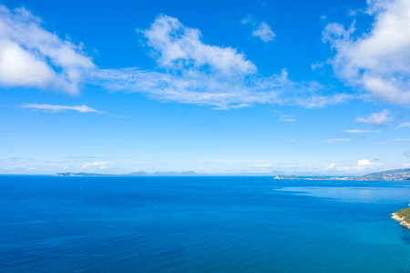 Expansive view of the deep blue Ionian Sea with a distant coastline and scattered clouds under a bright sky. The scene highlights the clarity and vivid color of the Mediterranean seascape.の写真素材