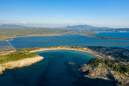 Sweeping aerial perspective reveals the iconic semicircular Voidokilia Beach with turquoise waters, golden sand, and rugged headlands along the Paleokastro coastline in Messinia, Greece. The tranquil Mediterranean landscape is framed by blue sky, coastal lagoons, and distant mountains.の写真素材