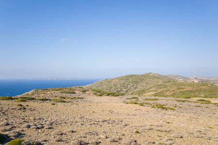 Arid rocky terrain stretches toward low green hills and the deep blue Mediterranean Sea under a clear sky in Crete. Sparse vegetation and distant islands create an open, tranquil landscape.の写真素材