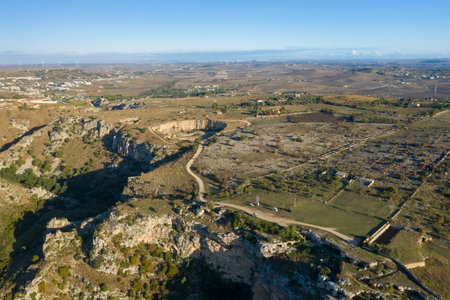 Expansive aerial view of rugged cliffs and open countryside on the outskirts of Matera, Italy, with winding dirt roads and patchwork fields under a clear blue sky.の写真素材