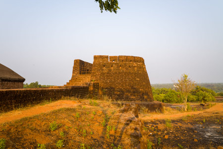 A robust stone bastion rises above sunlit fort walls at Bekal Fort, India, surrounded by dry earth...