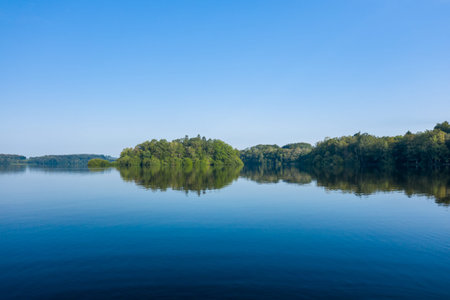 Bright morning sunlight illuminates the still waters of Lac des Settons, perfectly mirroring a...