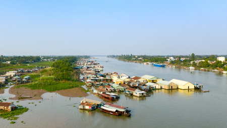 Aerial perspective of a floating village on the river near Chau Doc, Vietnam, with clusters of colorful houses and boats anchored along the water. The scene features lush green banks, open sky, and the unique architecture of riverside settlements in Southeast Asia.の写真素材