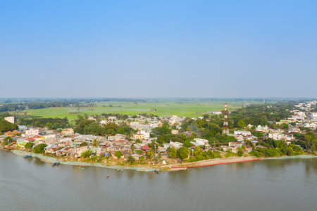 Wide aerial view of Chau Doc village along the river, with clustered houses, lush greenery, and...