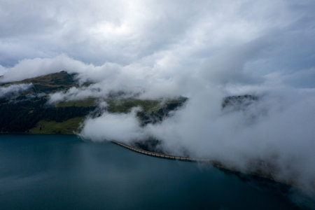 Thick clouds drift over the curved structure of Roselend Dam and the deep blue waters of the alpine...