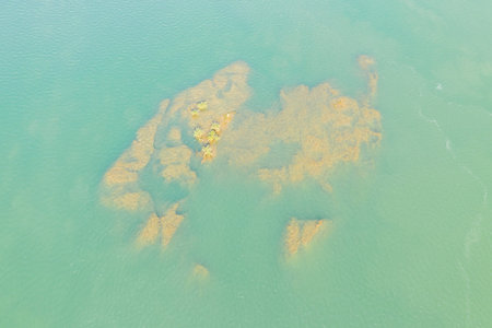 Sunlit rocks and small shrubs appear beneath the clear turquoise water of the Mekong River near...