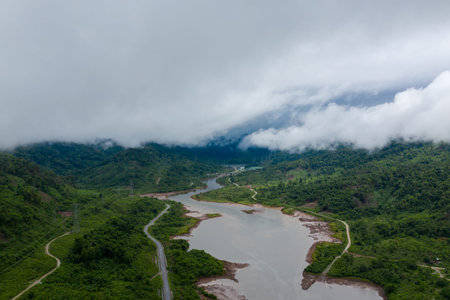Aerial perspective of a winding river bordered by lush green hills and partially obscured by...