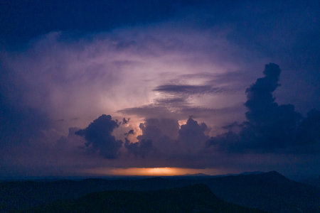 Dark storm clouds tower above a distant mountain ridge, glowing with flashes of lightning in the...