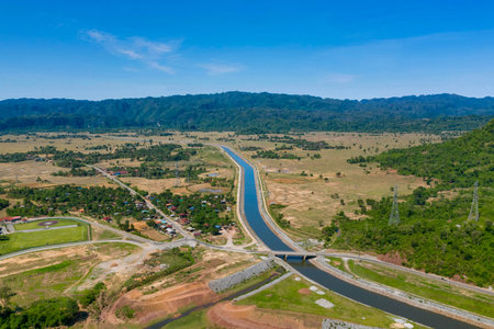 Wide aerial perspective shows a straight canal running through an open rural valley bordered by...