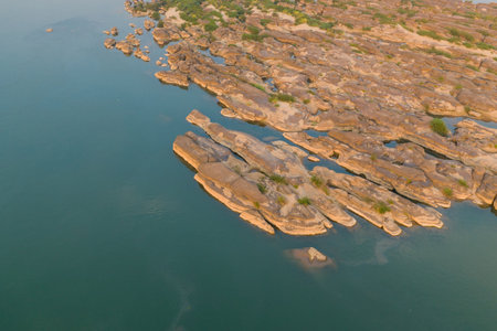 Aerial perspective of smooth sandstone outcrops and scattered vegetation along the tranquil Mekong River near Champassak in southern Laos. Warm daylight reveals natural patterns, gentle water, and subtle textures in this expansive river landscape.の写真素材