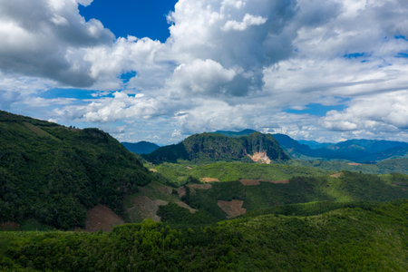 A wide green plateau rises between forested hills and steep cliffs beneath a sky filled with textured cumulus clouds in the countryside between Phou Khoun and Luang Prabang, northern Laos. The landscape features patchwork vegetation, open slopes, and distant blue ridges under vibrant daylight.の写真素材
