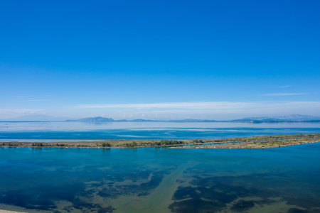 Expansive view of the Missolonghi salt lagoon in western Greece, featuring calm blue water, a narrow...
