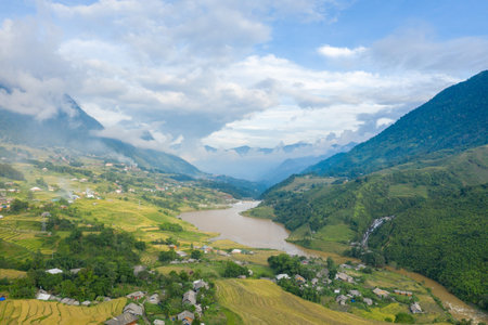 Aerial view of a winding river cutting through lush terraced rice fields and scattered rural houses...