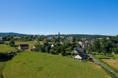 Drone perspective of a charming rural village surrounded by green fields and rolling hills, with a...