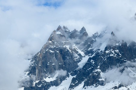 Steep, jagged peaks of Aiguille de Blaitiere rise through drifting clouds, with streaks of snow clinging to rugged rock faces in the French Alps.の写真素材
