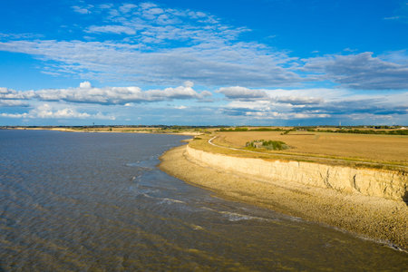 Wide view of pale limestone cliffs rising above a rocky shoreline and golden fields along the...