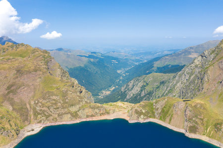 Expansive aerial perspective over Lac Bleu in the Pyrenees, with steep grassy ridges and rugged...
