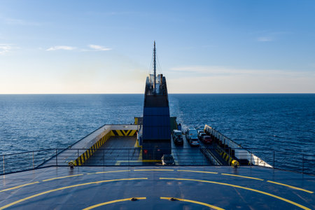 Wide angle view from the upper deck of a ferry shows geometric safety markings and vehicles below, with open blue water stretching to the horizon under clear daylight. The scene highlights maritime travel between the Adriatic and Ionian Seas, featuring crisp lines and a tranquil seascape.の写真素材