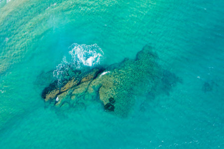 Aerial shot of a rocky reef beneath transparent turquoise sea near Acciaroli, Italy. Sunlight...