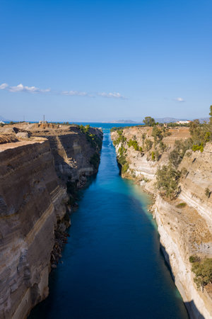 Long perspective of the Corinth Canal with deep blue water flowing between steep limestone cliffs,...