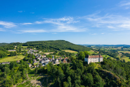 Wide drone view of Larochemillay village nestled among rolling green hills and dense forest, with a...