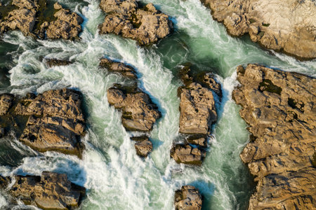 Detailed aerial view of swirling whitewater rushing between rugged rocks at Chutes de Khone on the Mekong River in southern Laos. The textured stone and dynamic water patterns highlight the raw energy of the cascade.の写真素材