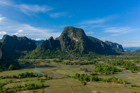 Dramatic karst mountains rise above a patchwork of green fields and scattered water pools in the...