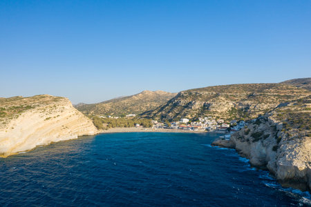 Vivid aerial view of Matala bay in Crete, showing turquoise water bordered by pale limestone cliffs...