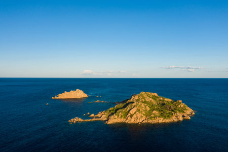 Two rugged rocky islets with patches of green vegetation rise from deep blue Mediterranean waters...