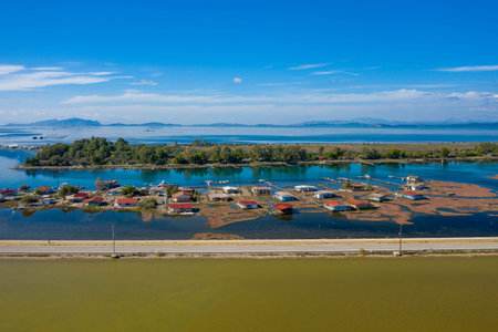 Colorful stilt houses line the edge of Tourlida lagoon in western Greece, surrounded by calm blue...