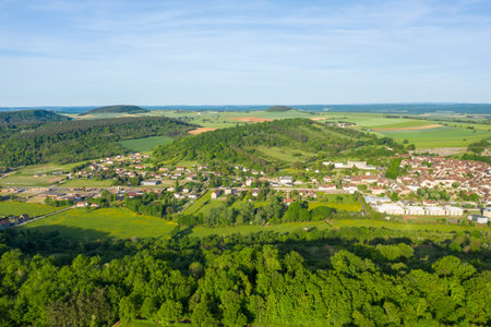 High-angle view of Varzy village surrounded by rolling hills, dense forests, and patchwork farmland under a clear blue sky in spring, showcasing vibrant rural scenery.の写真素材