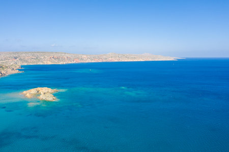 Aerial view of vibrant turquoise waters and a small rocky islet off the arid coastline near Vai beach. The clear blue sky and expansive seascape create a bright, inviting summer atmosphere.の写真素材