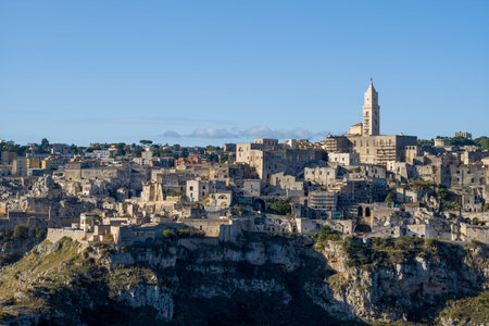 Historic stone buildings and the cathedral tower of Matera, Italy, rise above dramatic cliffs,...