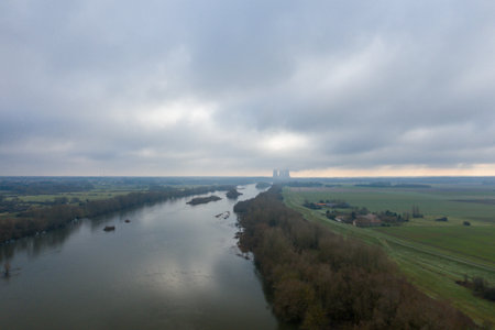 Aerial perspective of the Loire river curving between winter fields and bare trees under a dramatic cloudy sky near Dampierre. The muted light and distant horizon evoke a sense of quiet solitude.の写真素材